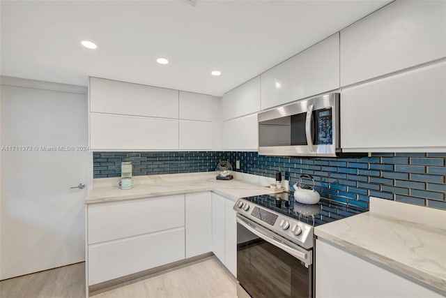 kitchen featuring light stone countertops, tasteful backsplash, light hardwood / wood-style floors, white cabinets, and appliances with stainless steel finishes