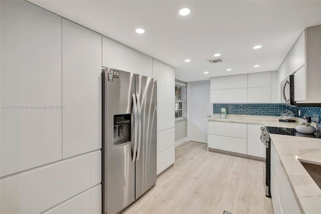 kitchen with light stone countertops, white cabinetry, stainless steel appliances, light hardwood / wood-style flooring, and decorative backsplash