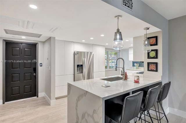 kitchen featuring kitchen peninsula, stainless steel refrigerator with ice dispenser, sink, decorative light fixtures, and white cabinets