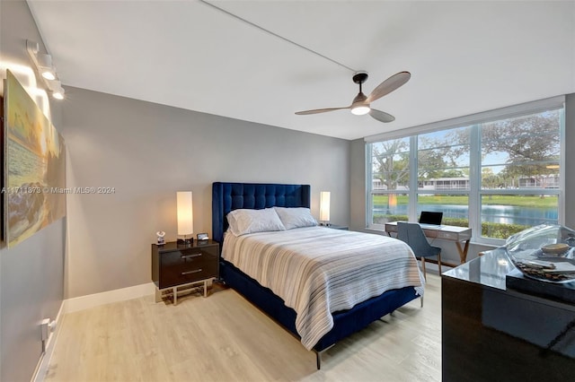 bedroom with hardwood / wood-style floors, a water view, and ceiling fan