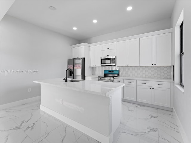 kitchen with decorative backsplash, stainless steel appliances, white cabinetry, and an island with sink