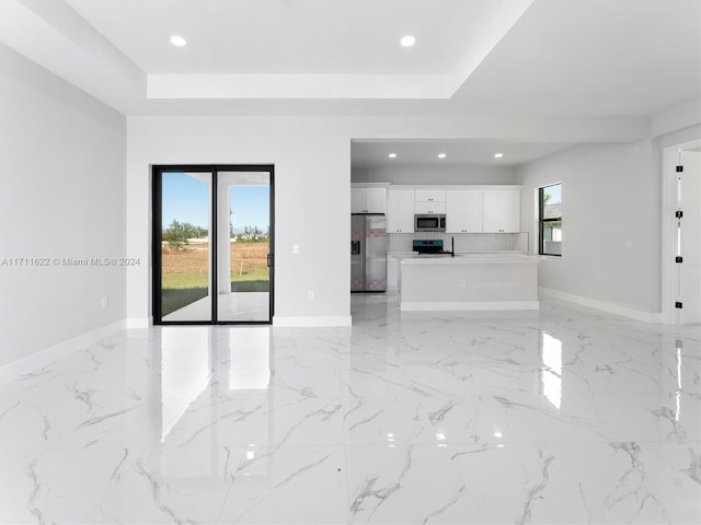 unfurnished living room featuring a raised ceiling and plenty of natural light