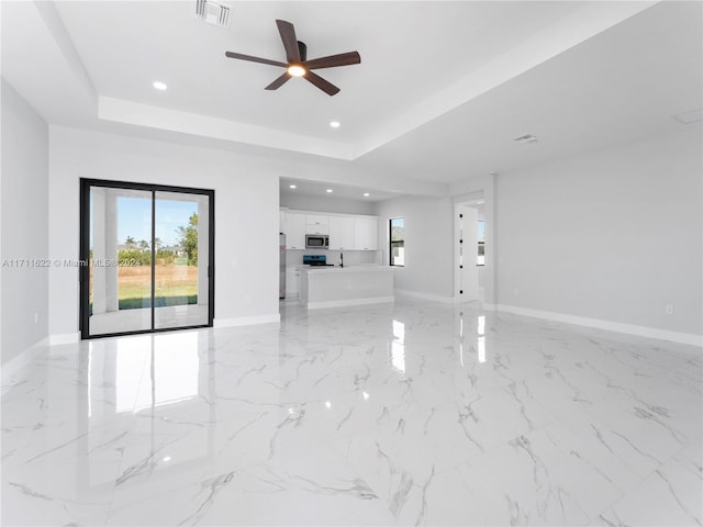 unfurnished living room featuring ceiling fan and a raised ceiling