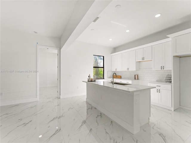 kitchen with white cabinets, decorative backsplash, sink, and an island with sink