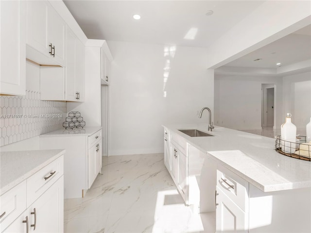 kitchen with decorative backsplash, white cabinetry, light stone countertops, and sink