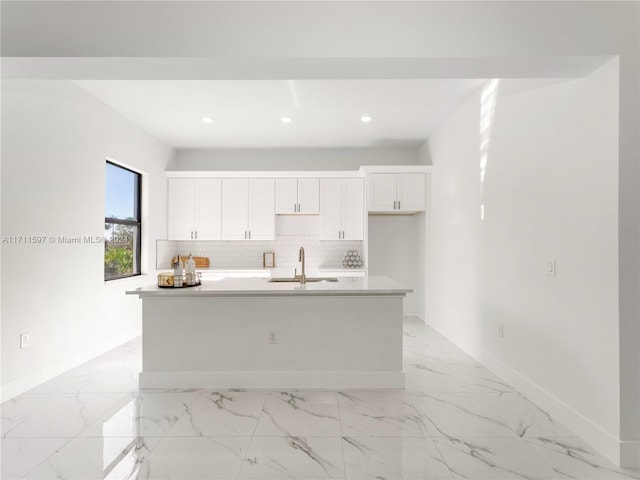 kitchen featuring white cabinets, decorative backsplash, sink, and an island with sink