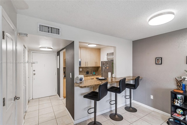 kitchen with light tile patterned floors, stainless steel refrigerator, light brown cabinetry, and light stone counters