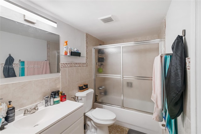 full bathroom featuring vanity, shower / bath combination with glass door, decorative backsplash, toilet, and tile walls