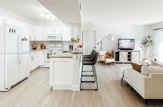 kitchen with a kitchen breakfast bar, white appliances, white cabinetry, and open floor plan