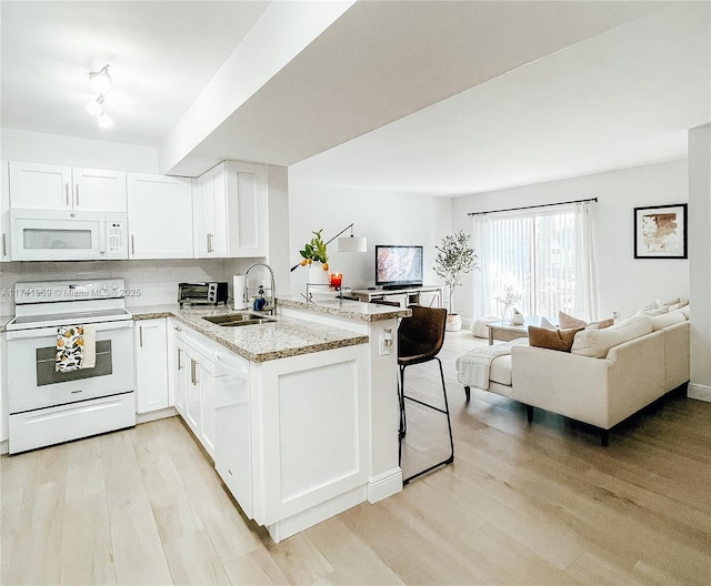 kitchen featuring open floor plan, a peninsula, white appliances, and white cabinetry