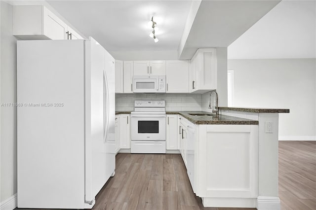 kitchen featuring white appliances, decorative backsplash, white cabinets, a peninsula, and a sink