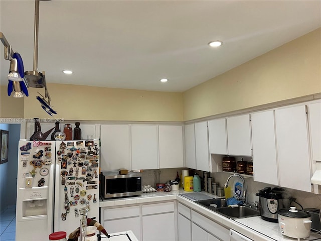 kitchen featuring sink, white refrigerator with ice dispenser, tile countertops, and white cabinetry