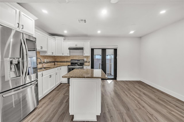 kitchen with appliances with stainless steel finishes, light hardwood / wood-style floors, a kitchen island, and dark stone countertops