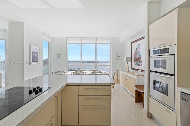 kitchen featuring stainless steel appliances, light tile patterned floors, kitchen peninsula, cream cabinetry, and a water view