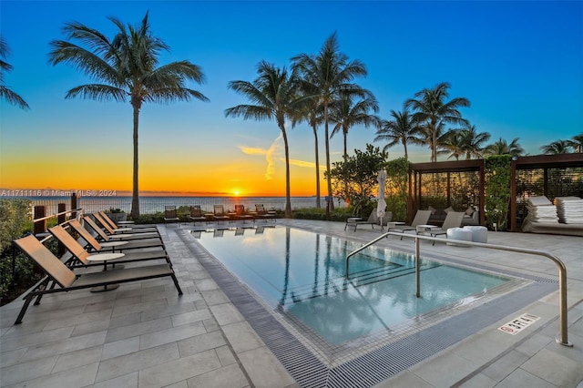 pool at dusk featuring a water view and a patio