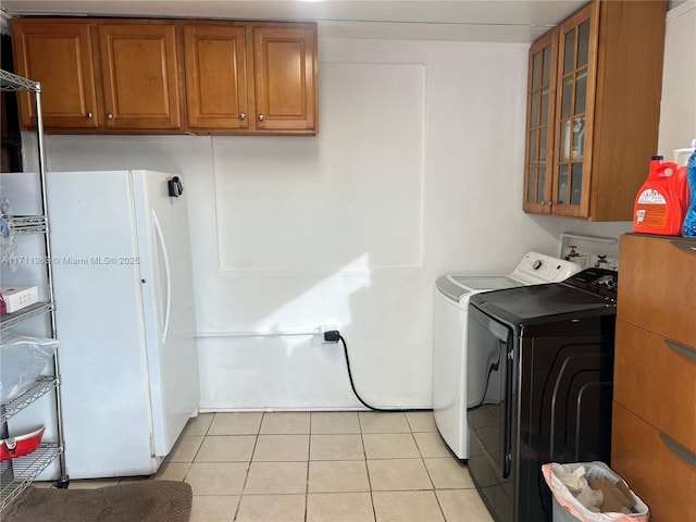 clothes washing area with cabinets, washer and dryer, and light tile patterned floors