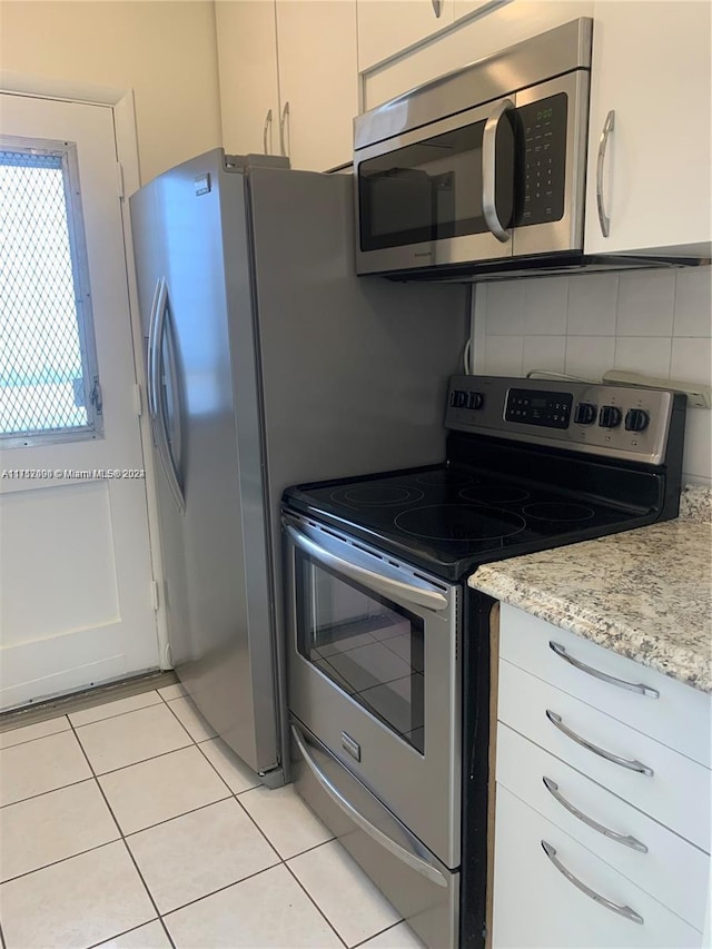 kitchen featuring backsplash, light stone counters, stainless steel appliances, light tile patterned floors, and white cabinetry