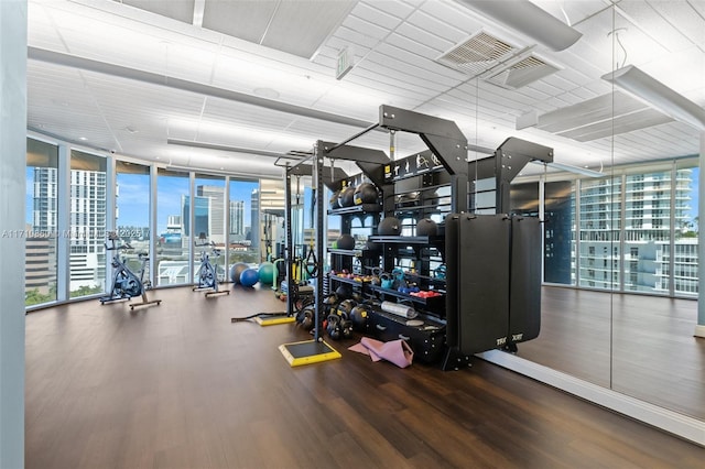 exercise room with a view of city, floor to ceiling windows, and wood finished floors