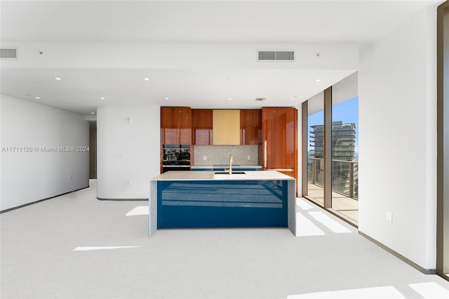 kitchen with backsplash, a center island with sink, and sink