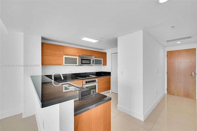 kitchen with kitchen peninsula, appliances with stainless steel finishes, light tile patterned floors, and sink