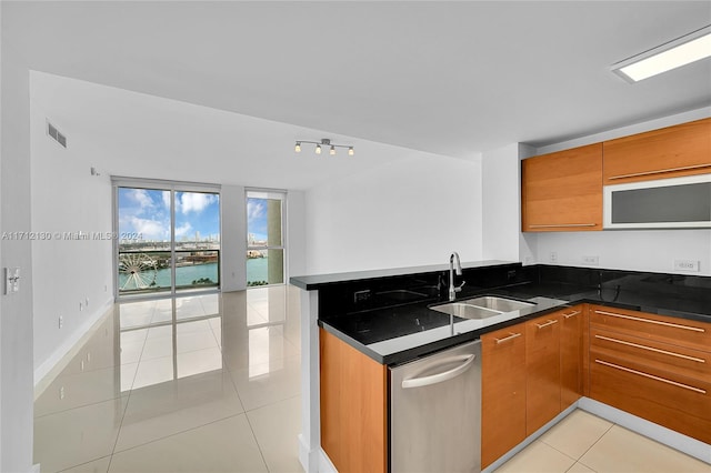 kitchen featuring dishwasher, sink, light tile patterned floors, dark stone counters, and a water view