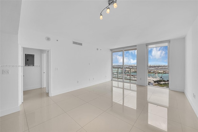 tiled empty room featuring expansive windows, a water view, and electric panel