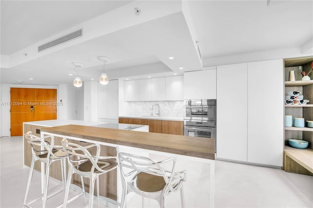 kitchen with pendant lighting, sink, a breakfast bar, white cabinets, and decorative backsplash