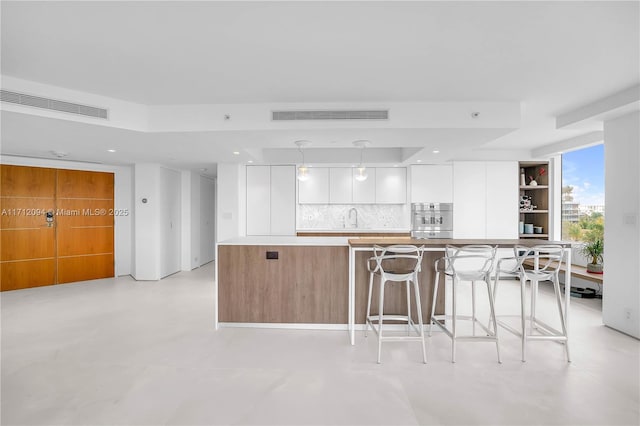 kitchen with sink, a breakfast bar area, white cabinetry, pendant lighting, and backsplash