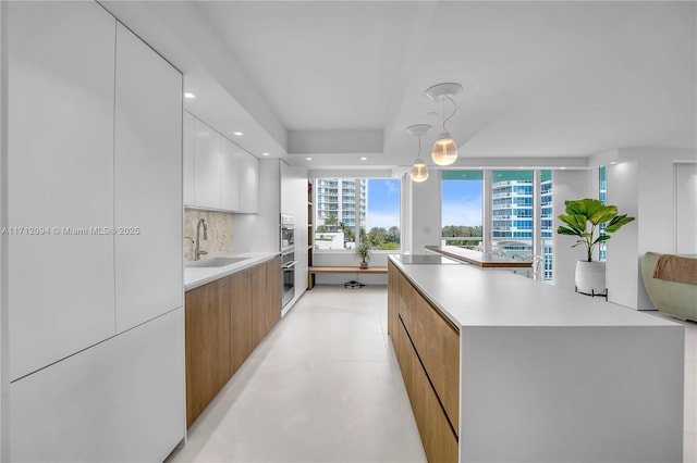 kitchen featuring sink, hanging light fixtures, a spacious island, white cabinets, and decorative backsplash