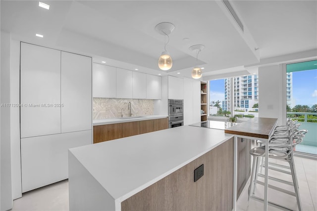 kitchen with sink, decorative light fixtures, a large island, decorative backsplash, and white cabinets