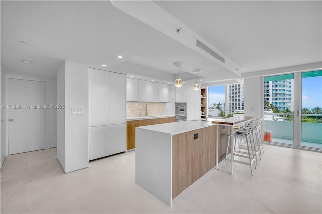 kitchen featuring a spacious island, sink, hanging light fixtures, decorative backsplash, and white cabinets