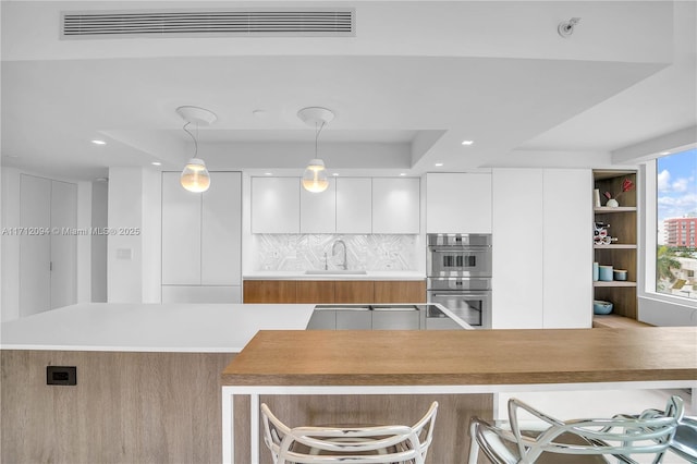 kitchen with pendant lighting, sink, white cabinetry, double oven, and tasteful backsplash