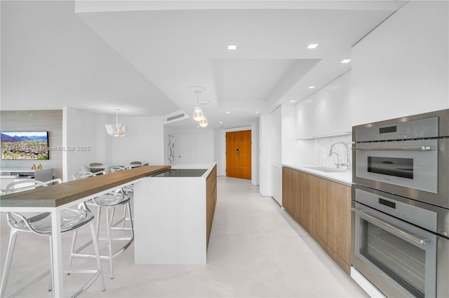 kitchen featuring decorative light fixtures, sink, white cabinets, a center island, and stainless steel double oven