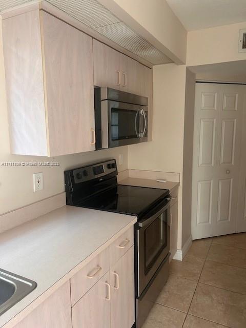 kitchen with light tile patterned floors, sink, light brown cabinetry, and black / electric stove