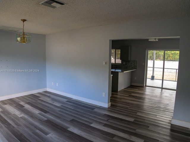 spare room featuring dark wood-type flooring, a textured ceiling, and a notable chandelier