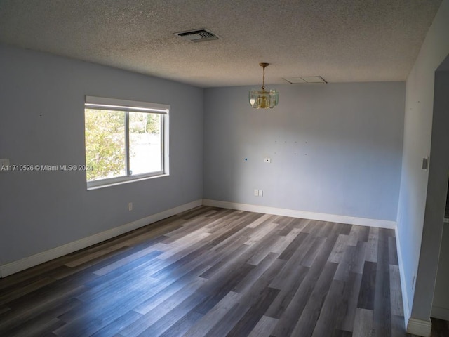 empty room featuring a textured ceiling, dark hardwood / wood-style floors, and an inviting chandelier