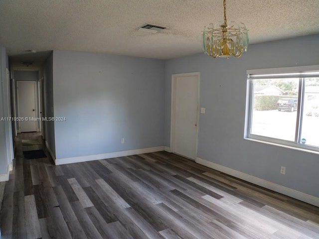 empty room featuring a textured ceiling, dark hardwood / wood-style floors, and a notable chandelier