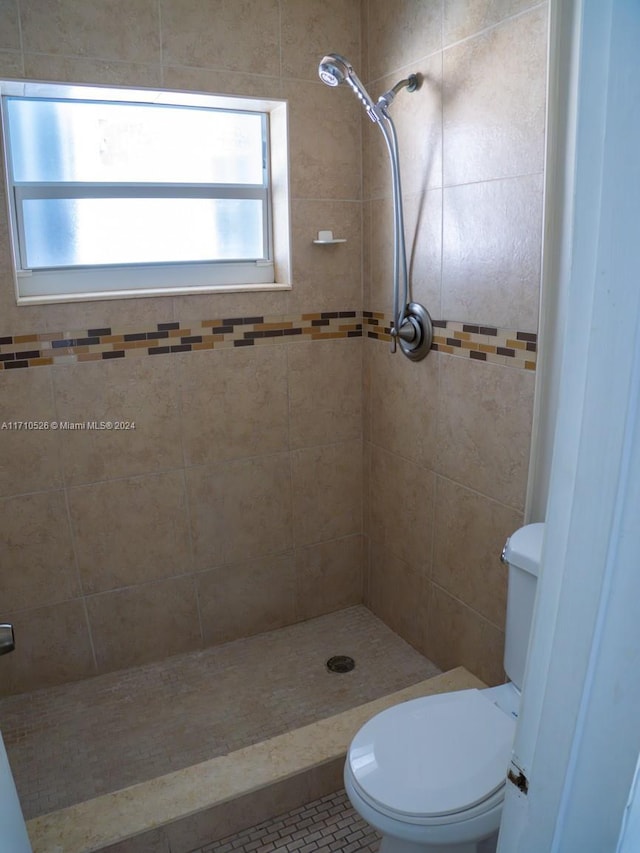 bathroom with toilet, tile patterned flooring, and tiled shower