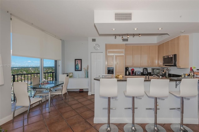 kitchen with dark tile patterned flooring, light brown cabinets, kitchen peninsula, and a breakfast bar area