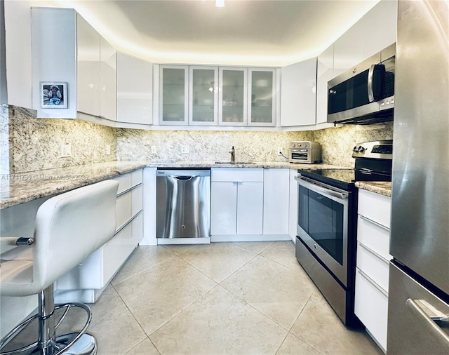 kitchen with light tile patterned floors, stainless steel appliances, white cabinets, light stone countertops, and modern cabinets