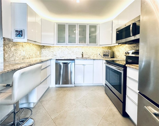 kitchen with white cabinetry, stainless steel appliances, light stone counters, backsplash, and light tile patterned floors