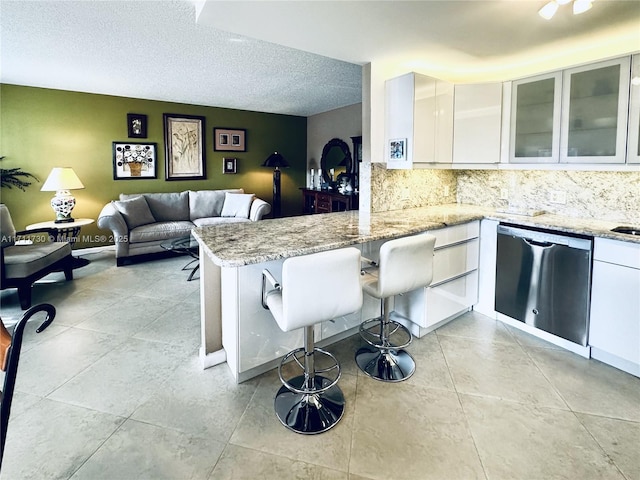 kitchen featuring kitchen peninsula, white cabinetry, dishwasher, and light stone counters