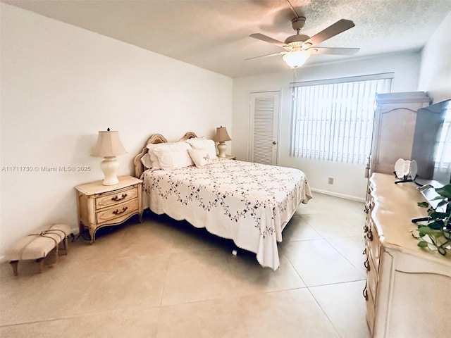 bedroom featuring a closet, light tile patterned flooring, ceiling fan, a textured ceiling, and baseboards