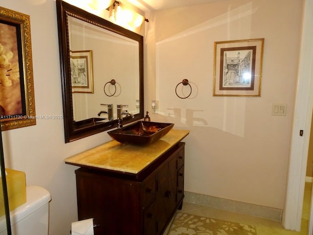 half bath with baseboards, vanity, toilet, and tile patterned floors