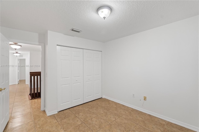 unfurnished bedroom featuring a closet, light tile patterned floors, and a textured ceiling