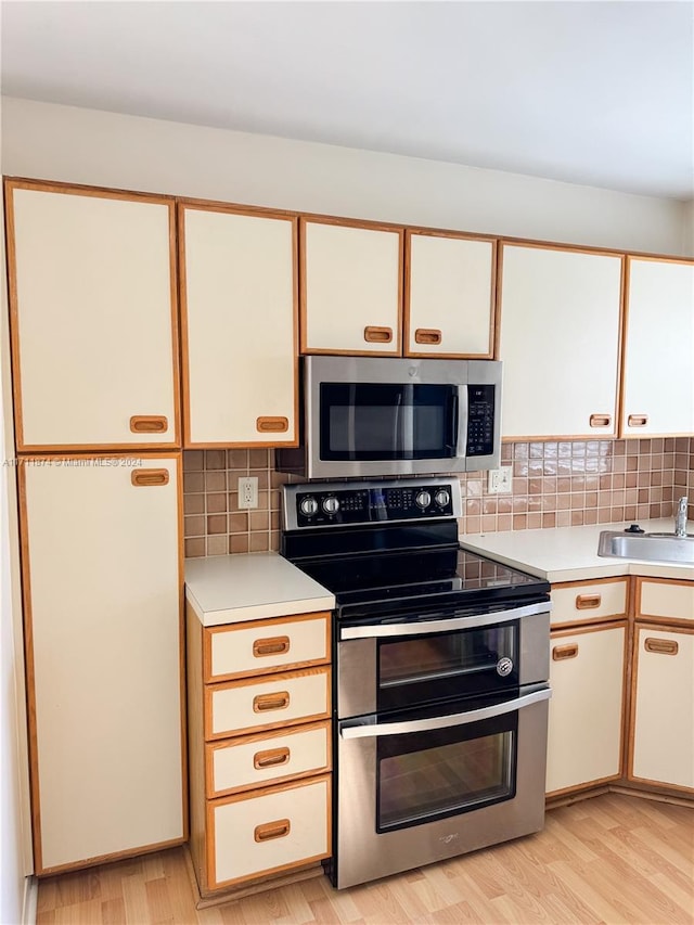 kitchen with sink, light wood-type flooring, appliances with stainless steel finishes, tasteful backsplash, and white cabinetry