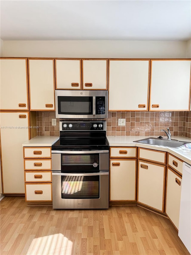 kitchen featuring a sink, light countertops, appliances with stainless steel finishes, decorative backsplash, and light wood finished floors