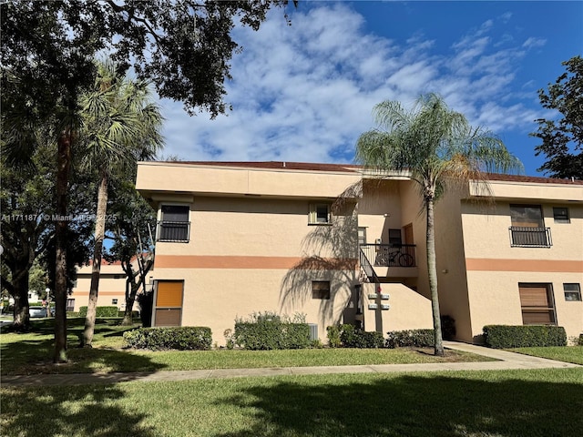 view of side of home featuring a yard, a balcony, and stucco siding