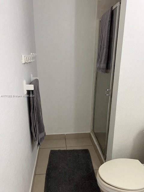 bathroom featuring toilet, tile patterned floors, and a shower with door