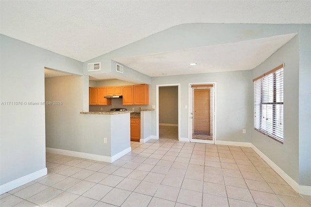 kitchen with vaulted ceiling, light tile patterned floors, light brown cabinetry, and light stone counters